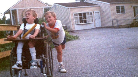 a photo scan of two children playing, one in a wheelchair and the other pushing him