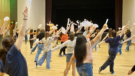 students in front of stage holding fans and following dance steps from people on the stage