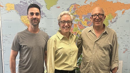 three people in a photo in front of a world map. The oregon governor is in the middle