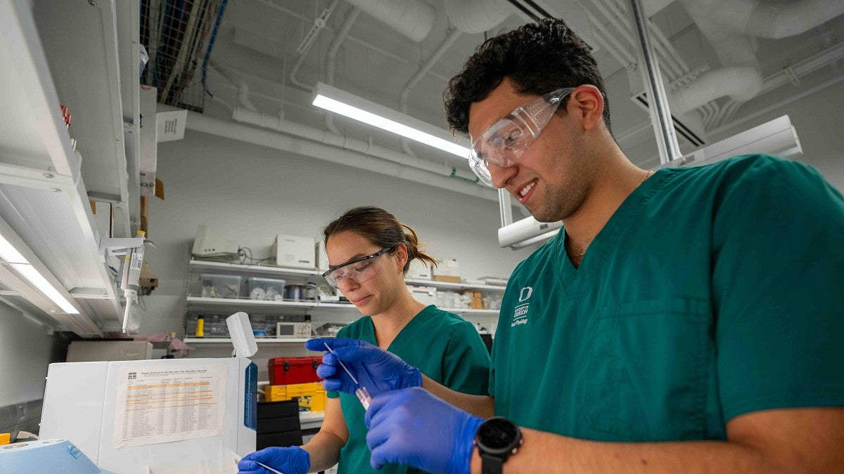 two students working in a lab wearing scrubs and safety glasses