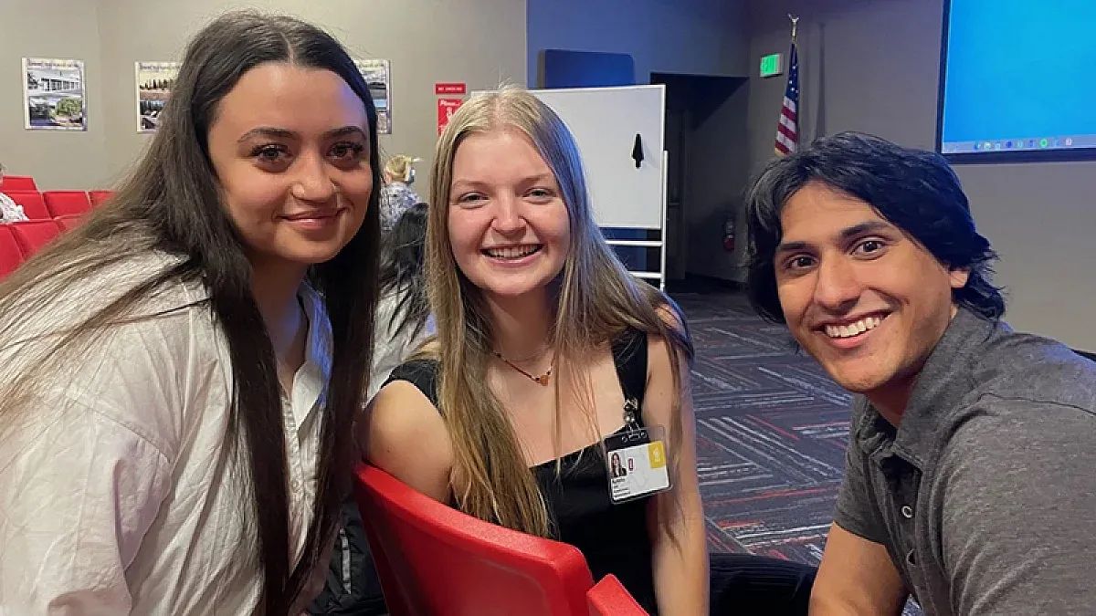 three students smiling while sitting in a conference room