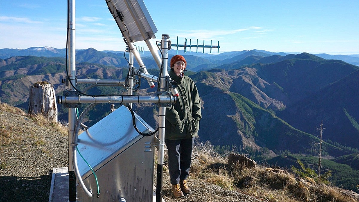 A person standing next to an antenna on a mountain