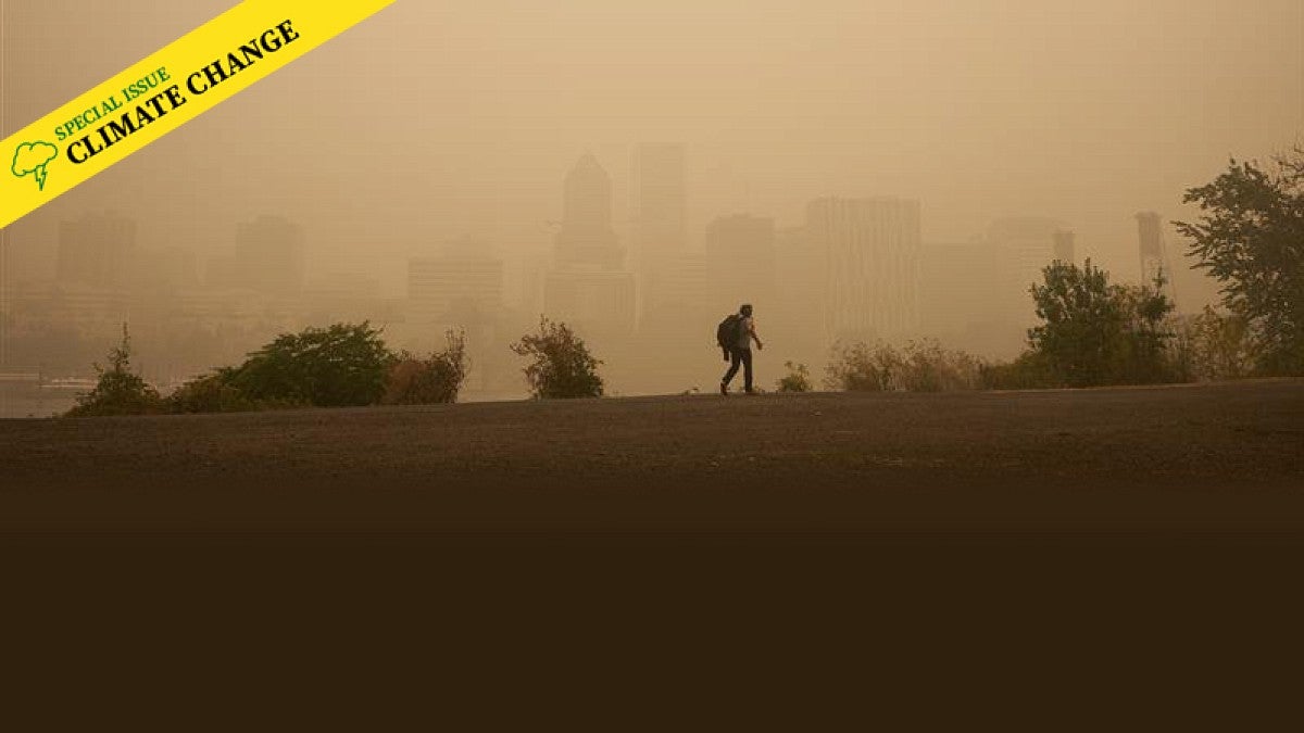 A person walking across a ridgeline with a city skyline in the background obscured by wildfire smoke