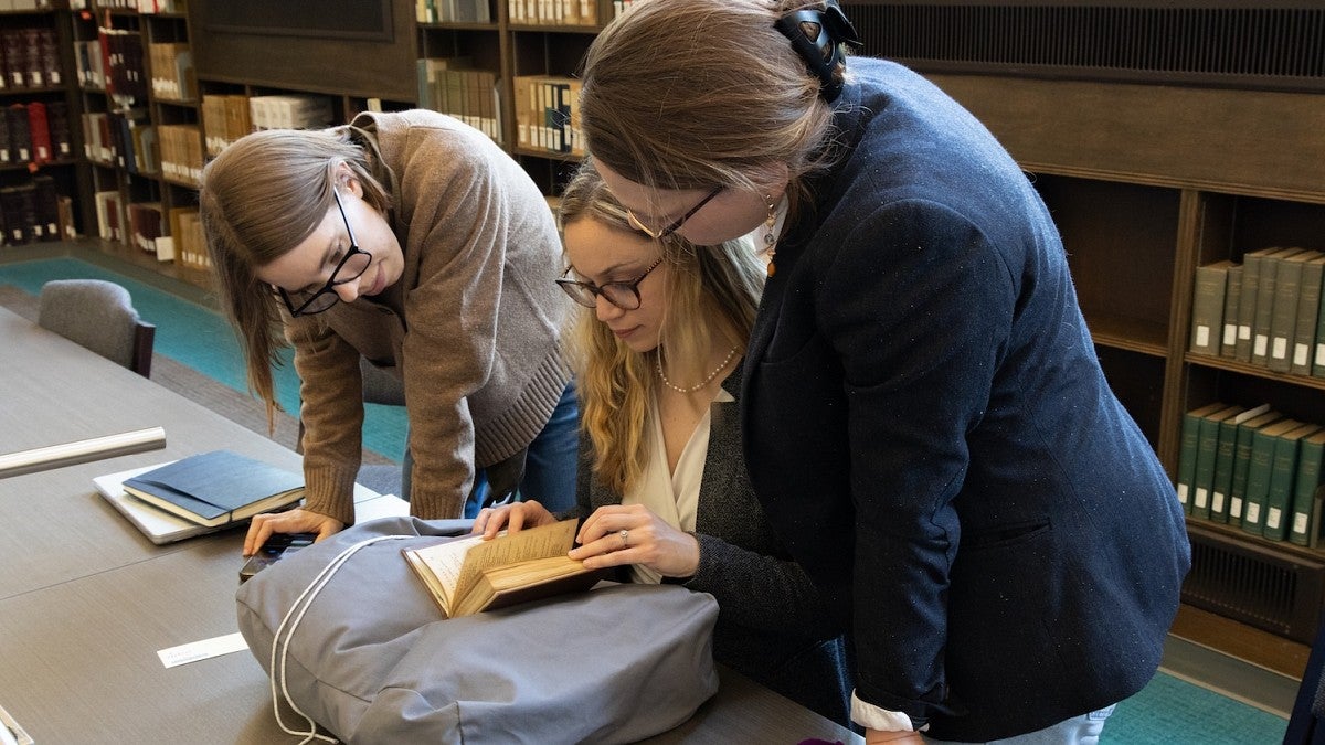 group of women looking at a book from an archive in the library
