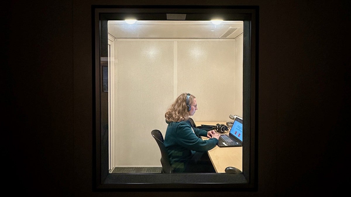 woman wearing headphones sitting in front of a computer in a sound booth