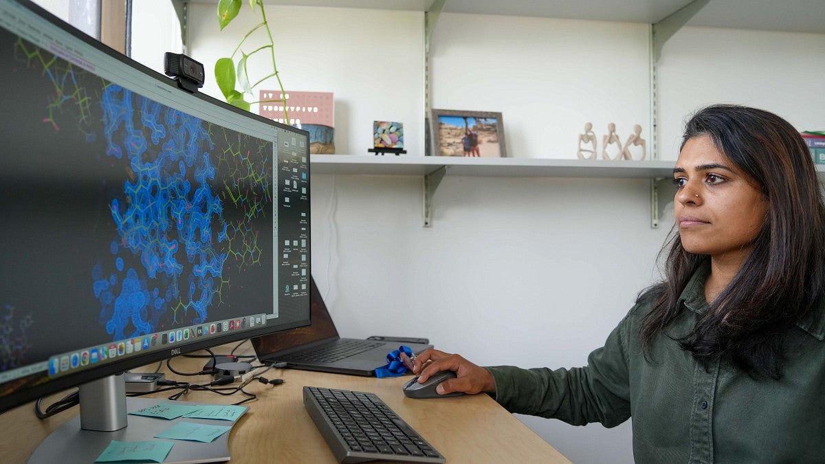 woman on the right sitting down facing a computer screen with a scene of cells