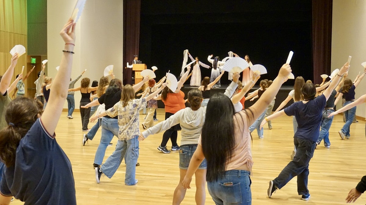students in front of stage holding fans and following dance steps from people on the stage