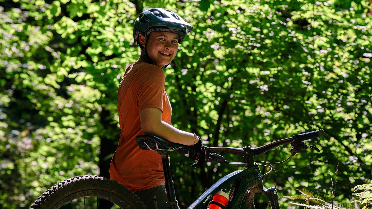 a person wearing a helmet carries a mountain bike on a trail